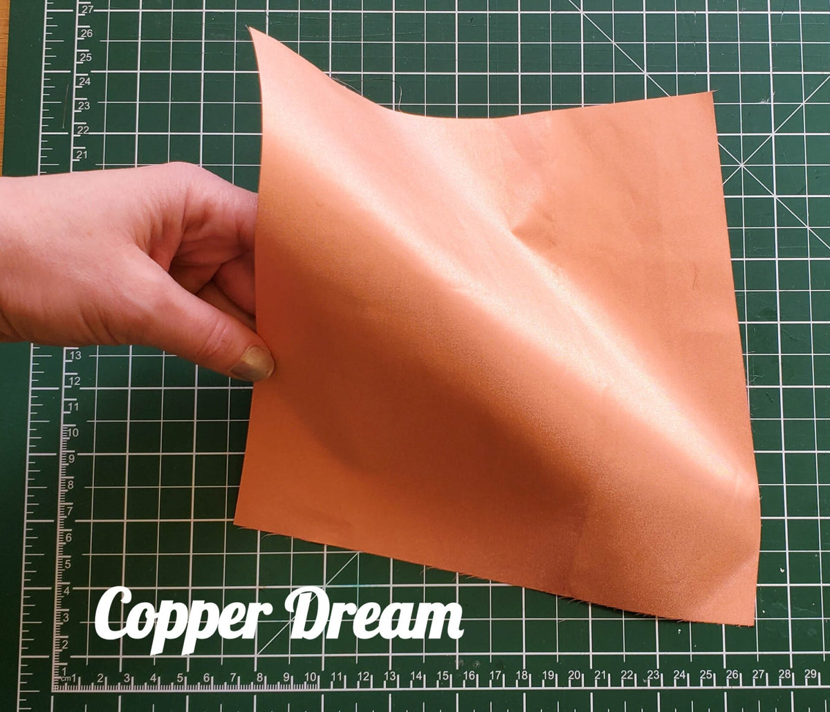 Hand holding a piece of copper conductive fabric on a cutting mat