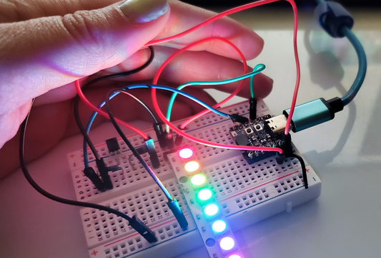 Hand holding a breadboard with LEDs and wires, connected to a microcontroller.