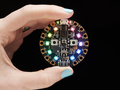 Circular electronic component with colorful LEDs held in a hand against a black background