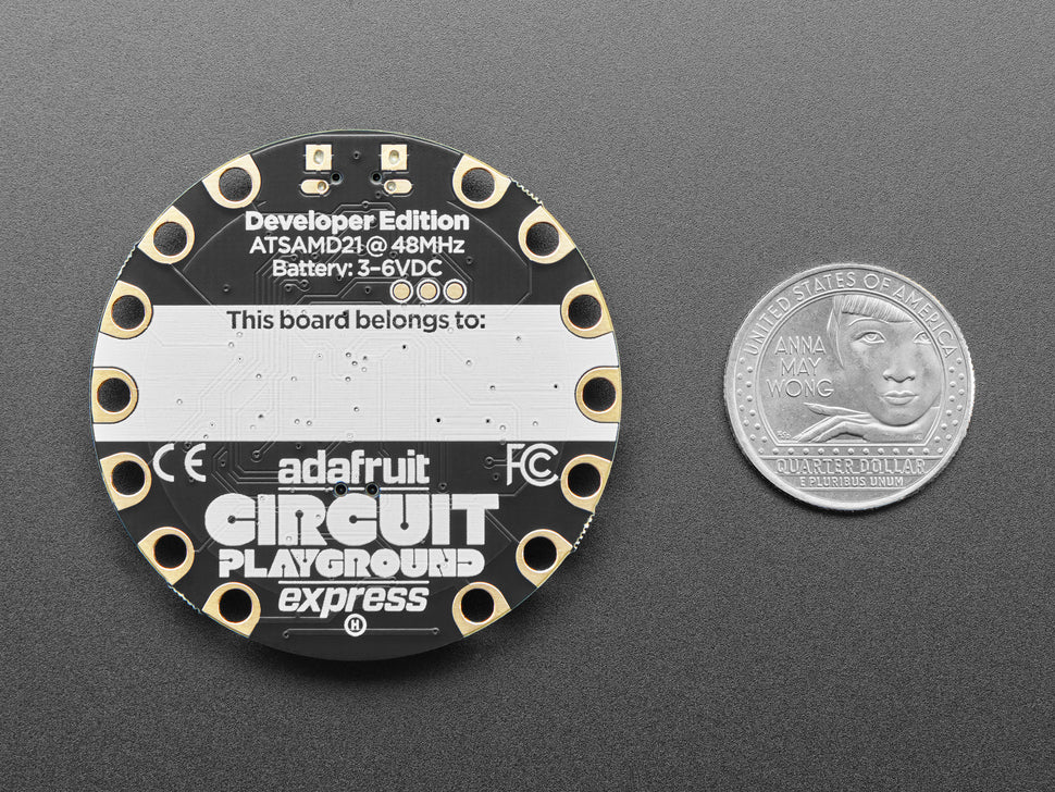 Adafruit Circuit Playground Express board with a quarter for scale on a gray background