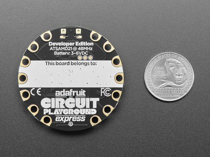 Adafruit Circuit Playground Express board with a quarter for scale on a gray background