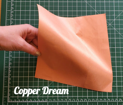 Hand holding a piece of copper conductive fabric on a cutting mat