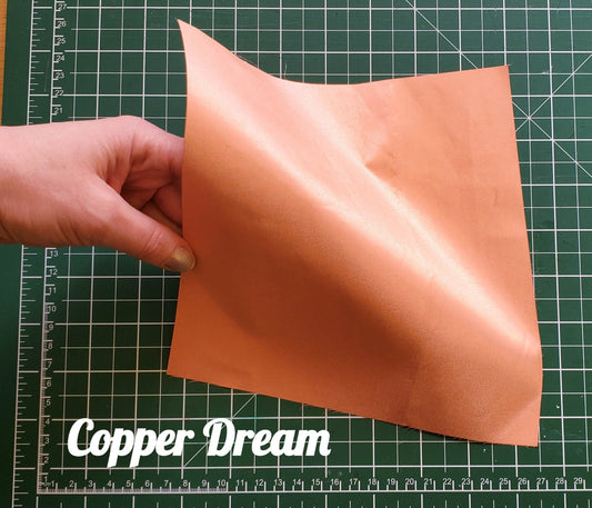 Hand holding a piece of copper conductive fabric on a cutting mat