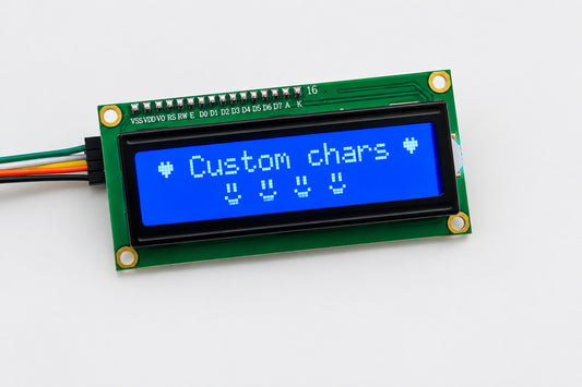 A small LCD display module with a green circuit board, a blue backlit screen showing the text 'Custom chars', and attached wires, photographed on a light tabletop.