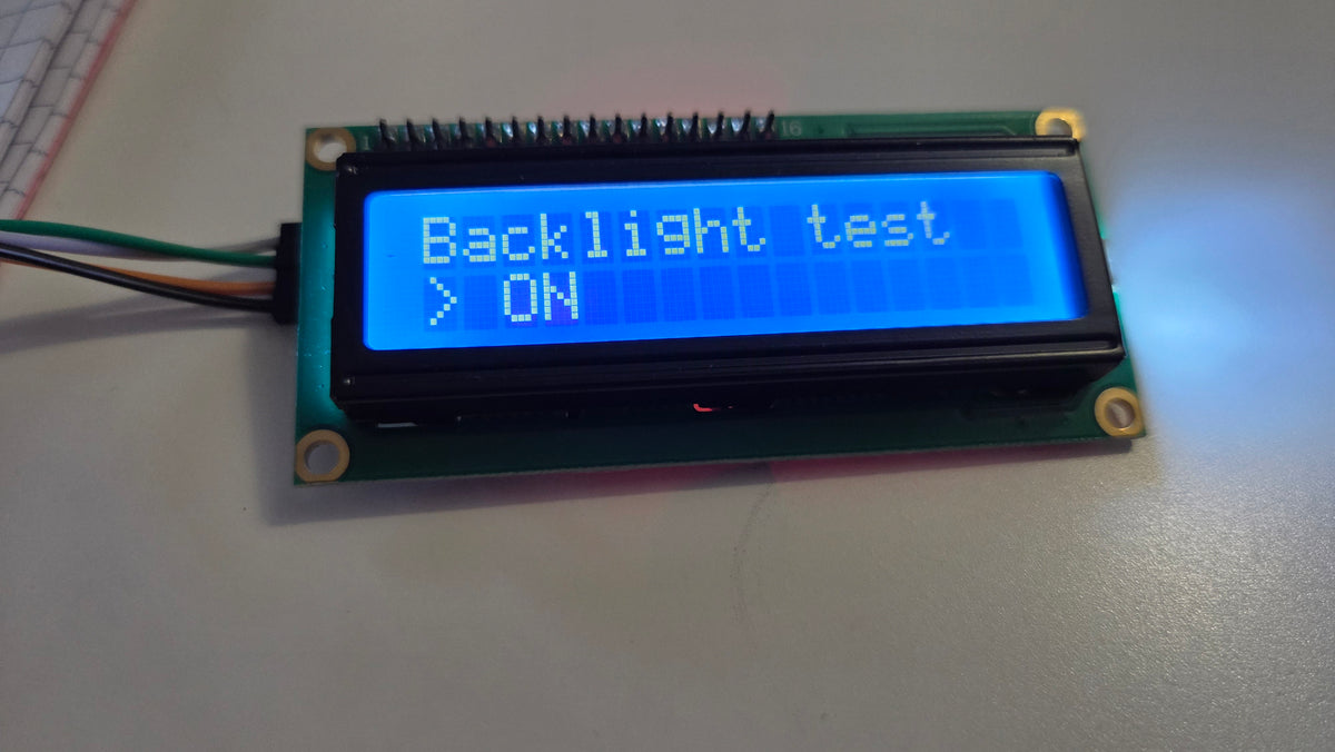 A small LCD display module with a blue backlit screen showing the text 'Backlight test > ON', photographed on a light tabletop.