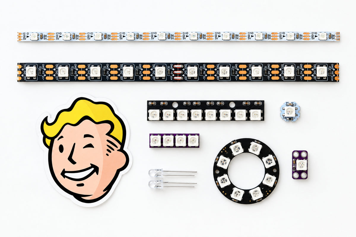 A DIY electronics kit laid out on a light gray surface, featuring an LED light strip, a printed circuit board with electronic components, a Fallout-style Vault Boy sticker, a clear tube, a black circular ring with white markings, and several small switches and connectors.
