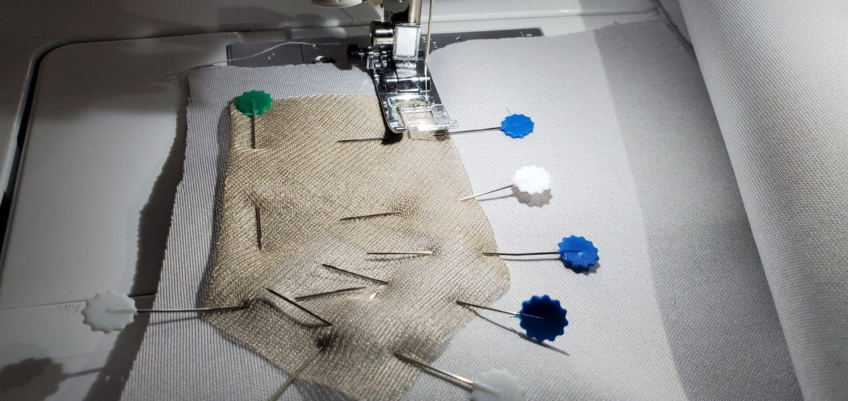 Silver conductive mesh fabric with blue snaps under a sewing machine